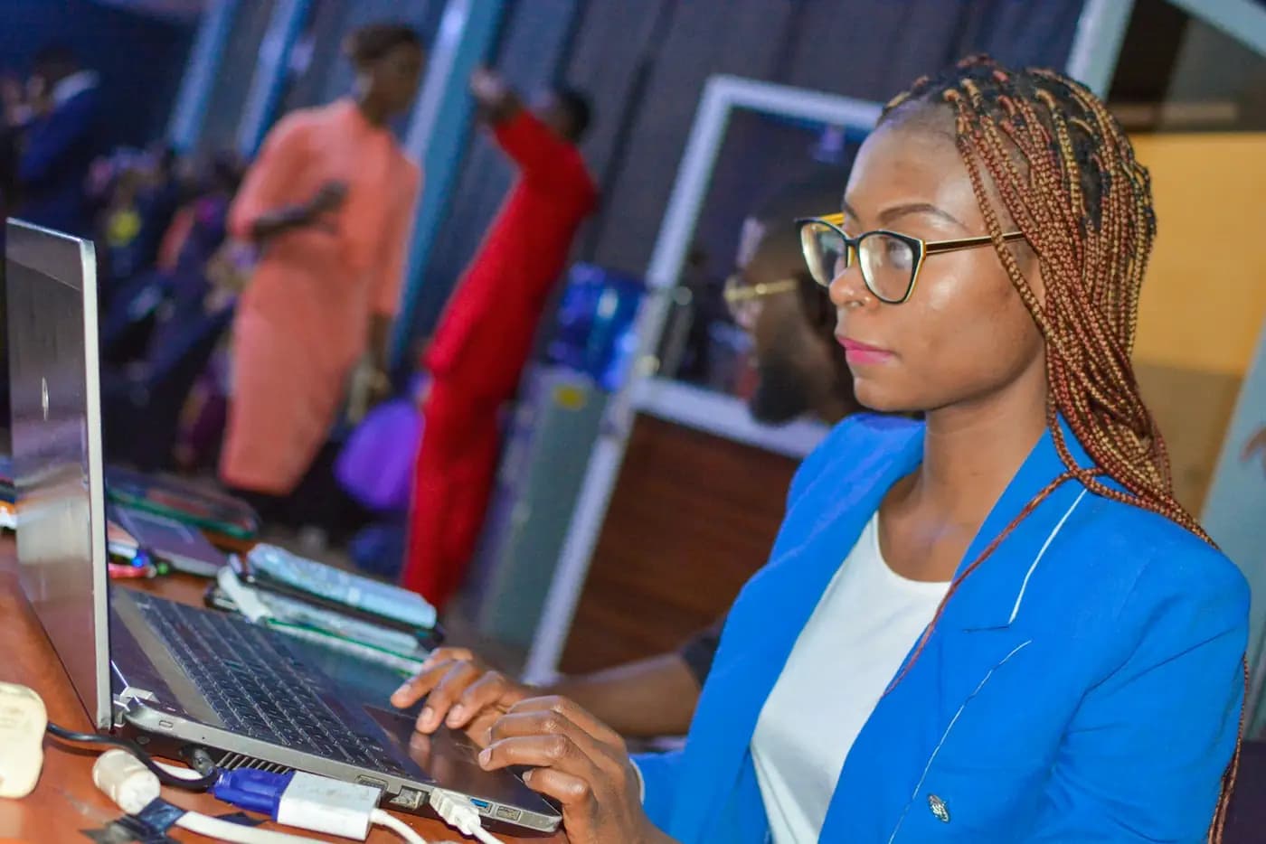 A planner working on her laptop during an event, with guests in traditional dress behind her