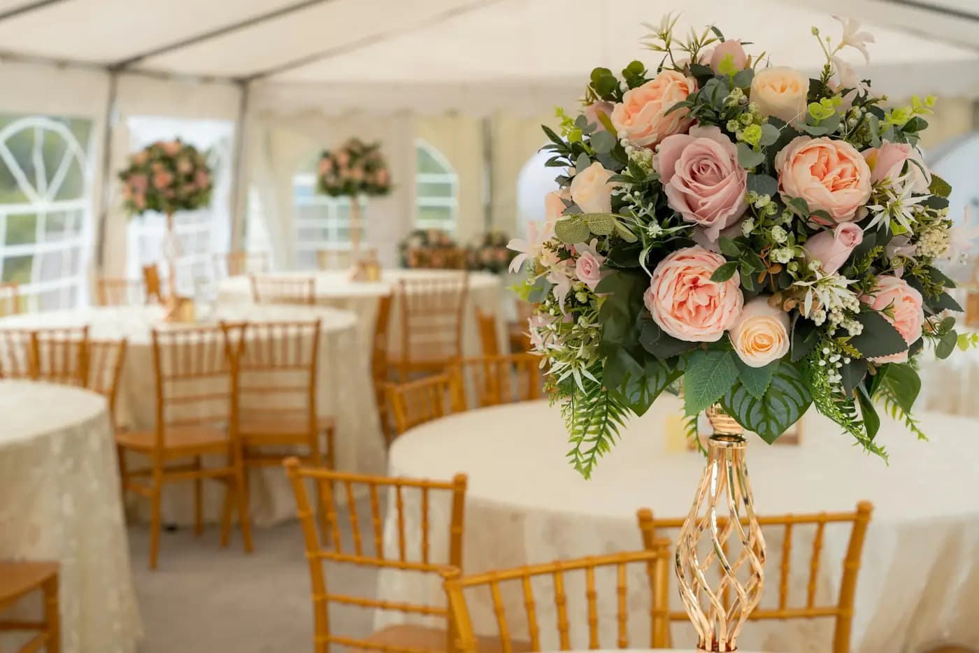 A reception under a marquee: round tables with cloths, gold chairs and floral centrepieces